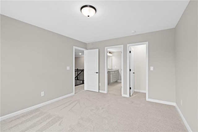 unfurnished bedroom with ensuite bath, light colored carpet, and baseboards