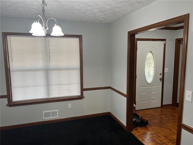 entryway featuring visible vents, a notable chandelier, a textured ceiling, and baseboards