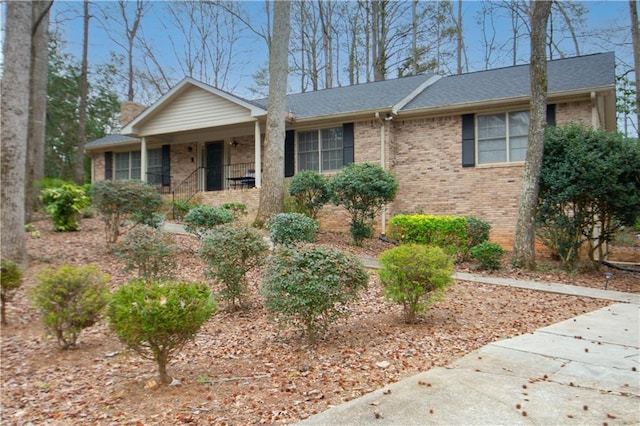 ranch-style house with roof with shingles, a porch, and brick siding