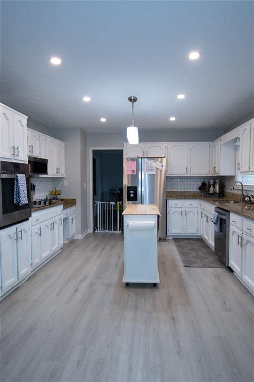 kitchen with a sink, white cabinets, appliances with stainless steel finishes, dark countertops, and decorative light fixtures