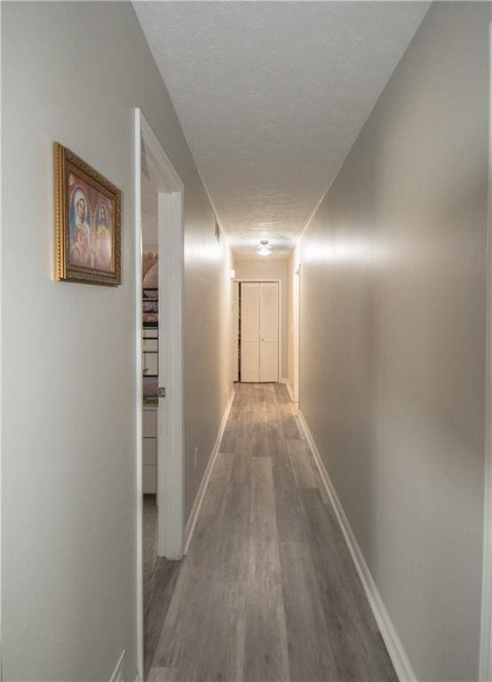 corridor with a textured ceiling, baseboards, and wood finished floors