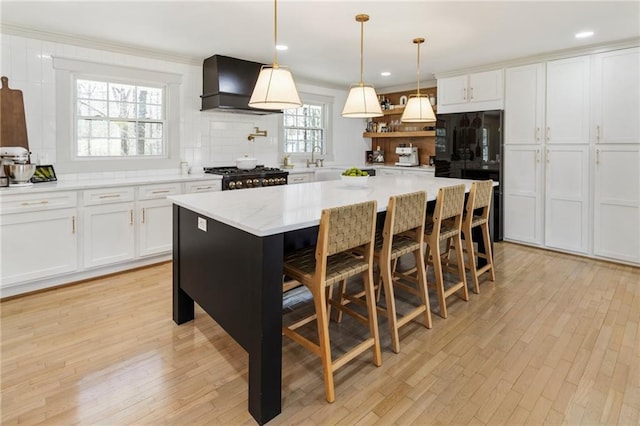 kitchen with tasteful backsplash, white cabinetry, wall chimney range hood, and stove