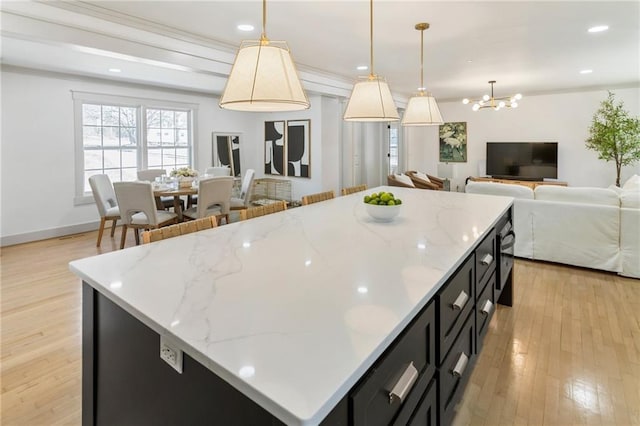 kitchen featuring light wood-style flooring, open floor plan, dark cabinets, a center island, and pendant lighting