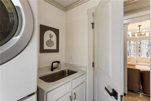 laundry area featuring stacked washer and clothes dryer, crown molding, cabinet space, an inviting chandelier, and a sink