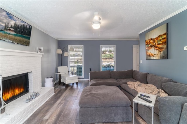 living area with a ceiling fan, wood finished floors, a fireplace, ornamental molding, and a textured ceiling