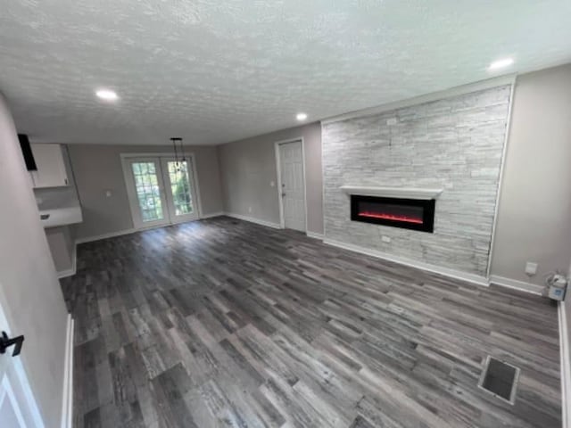 unfurnished living room with visible vents, a textured ceiling, wood finished floors, a fireplace, and baseboards