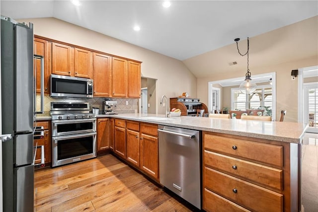 kitchen with sink, vaulted ceiling, appliances with stainless steel finishes, kitchen peninsula, and pendant lighting