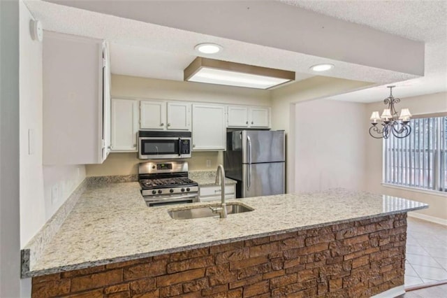 kitchen with a peninsula, a sink, white cabinets, appliances with stainless steel finishes, and pendant lighting