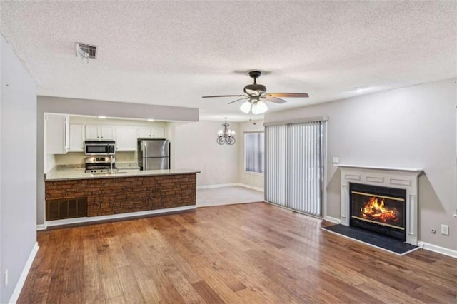 unfurnished living room with ceiling fan with notable chandelier, light wood-style flooring, a glass covered fireplace, and visible vents