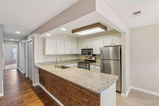 kitchen featuring light stone counters, appliances with stainless steel finishes, a sink, and white cabinetry