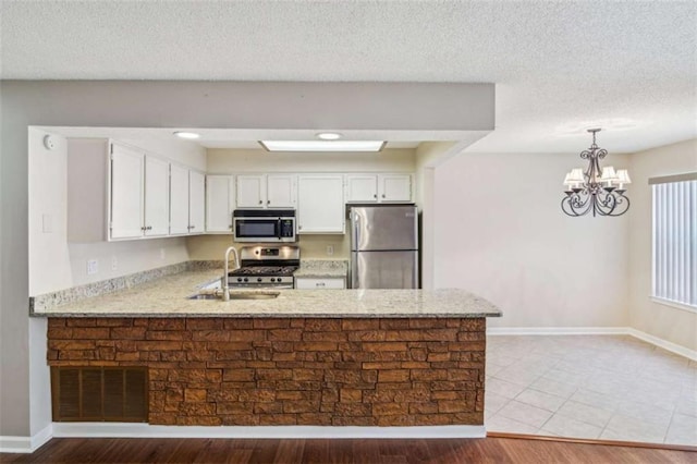 kitchen featuring a sink, white cabinetry, appliances with stainless steel finishes, light stone countertops, and decorative light fixtures