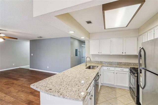 kitchen featuring stainless steel appliances, a peninsula, white cabinets, open floor plan, and light stone countertops