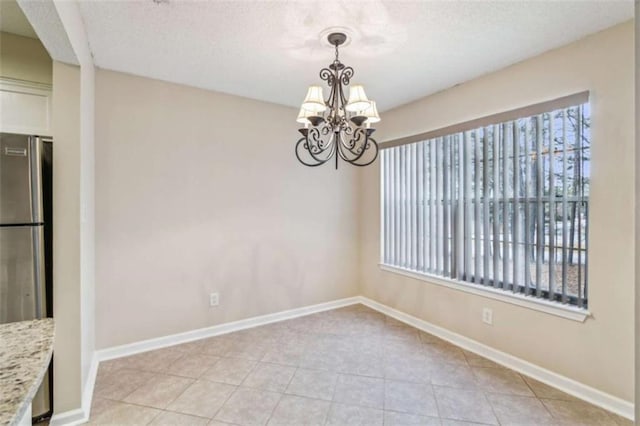 unfurnished dining area featuring baseboards, a chandelier, a textured ceiling, and light tile patterned flooring