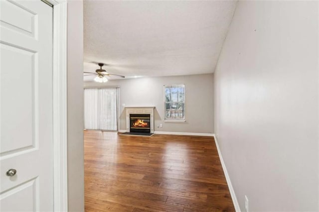 unfurnished living room with wood finished floors, a glass covered fireplace, a ceiling fan, and baseboards