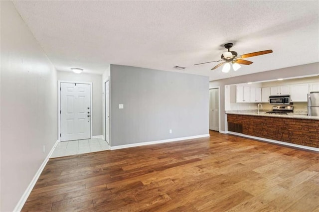 unfurnished living room featuring a textured ceiling, visible vents, baseboards, a ceiling fan, and light wood-style floors