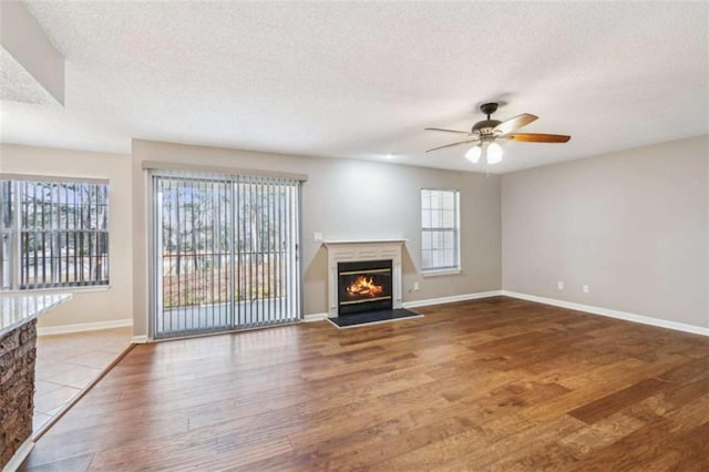 unfurnished living room featuring a ceiling fan, a glass covered fireplace, a textured ceiling, and wood finished floors