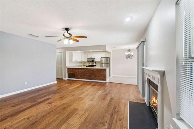 unfurnished living room featuring ceiling fan with notable chandelier, wood finished floors, a fireplace with flush hearth, visible vents, and baseboards