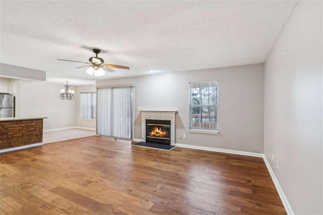 unfurnished living room featuring a glass covered fireplace, a textured ceiling, baseboards, and wood finished floors