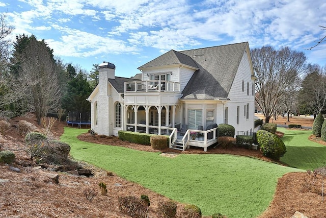 rear view of property with a balcony, a trampoline, a chimney, and a yard