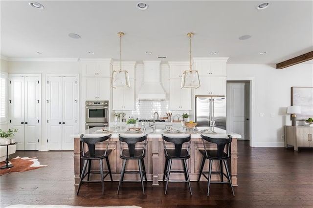 kitchen with premium range hood, a center island with sink, white cabinets, appliances with stainless steel finishes, and dark hardwood / wood-style flooring