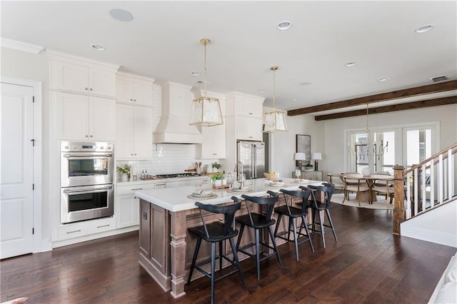 kitchen featuring a center island with sink, white cabinets, hanging light fixtures, dark hardwood / wood-style floors, and stainless steel appliances