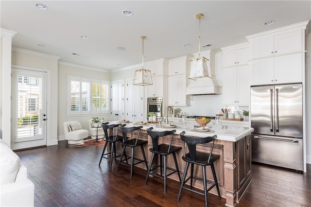 kitchen featuring premium range hood, stainless steel appliances, a kitchen island with sink, dark hardwood / wood-style floors, and hanging light fixtures