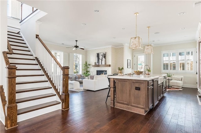 kitchen with a kitchen island with sink, crown molding, ceiling fan, decorative light fixtures, and dark hardwood / wood-style flooring