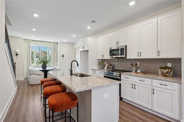 kitchen with appliances with stainless steel finishes, a kitchen island with sink, sink, and white cabinets