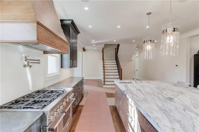 kitchen featuring premium range hood, sink, hanging light fixtures, high end stainless steel range, and light stone counters