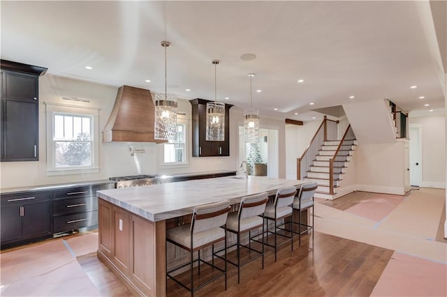 kitchen with a kitchen bar, sink, decorative light fixtures, custom range hood, and a large island