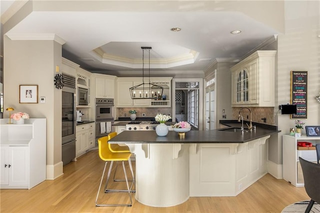 kitchen with dark countertops, glass insert cabinets, a peninsula, a tray ceiling, and a sink