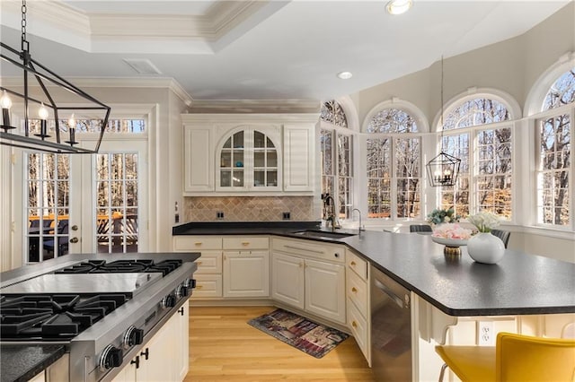 kitchen featuring stainless steel appliances, a sink, light wood-style floors, dark countertops, and an inviting chandelier