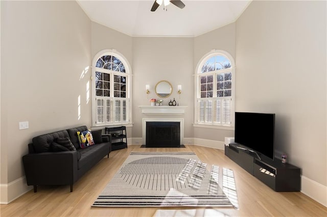 living room with a fireplace with flush hearth, a ceiling fan, baseboards, and wood finished floors