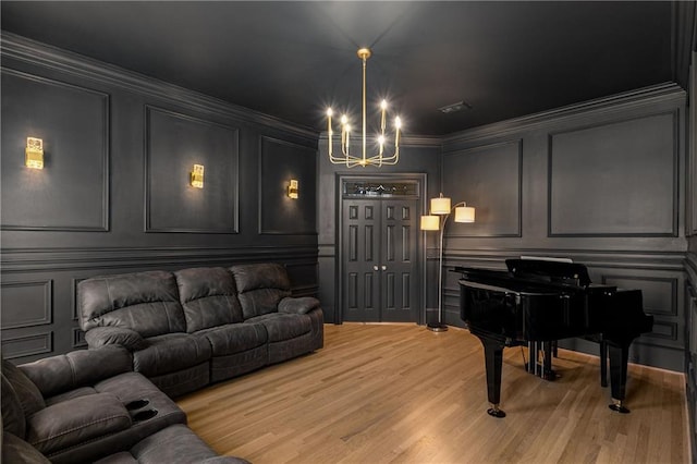 living area featuring crown molding, light wood-type flooring, a decorative wall, and an inviting chandelier