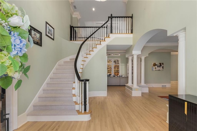 entrance foyer with baseboards, a high ceiling, wood finished floors, and ornate columns