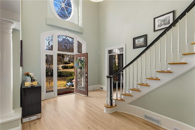 entryway with visible vents, a towering ceiling, wood finished floors, ornate columns, and stairs