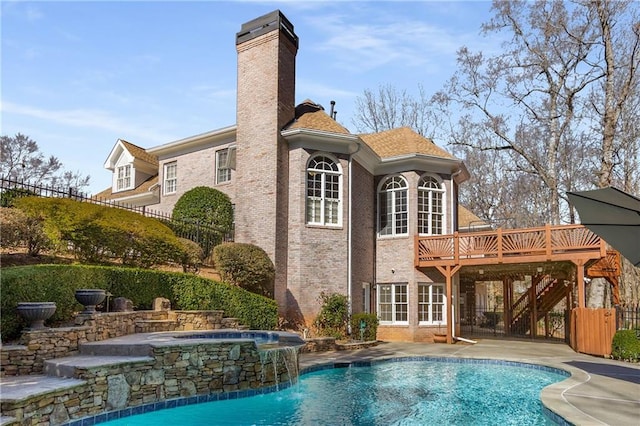 back of property with an in ground hot tub, brick siding, a wooden deck, a fenced in pool, and a chimney