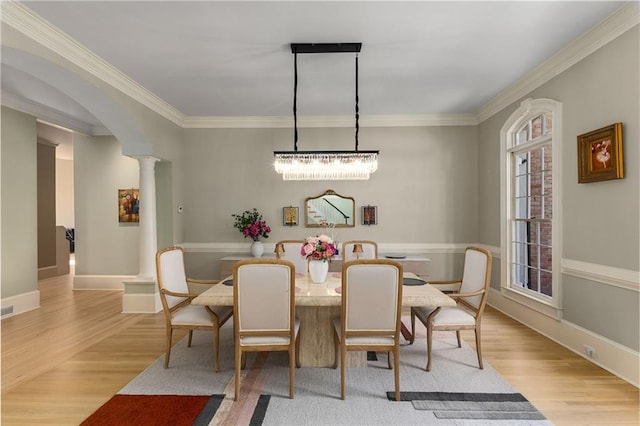 dining room featuring arched walkways, crown molding, decorative columns, and light wood-style floors