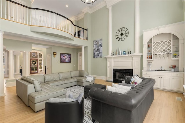 living area featuring light wood finished floors, a fireplace, indoor wet bar, and ornate columns