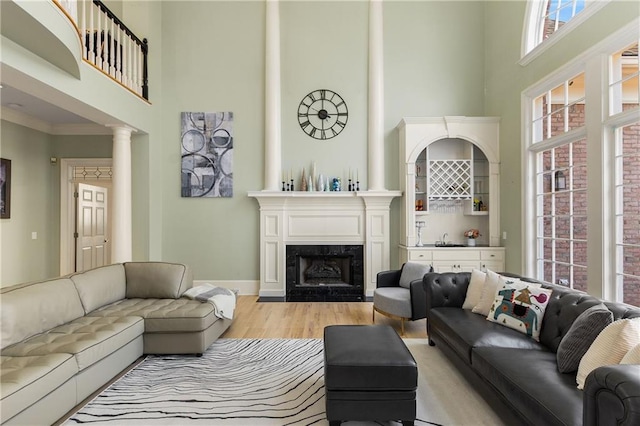 living room featuring ornate columns, a towering ceiling, light wood finished floors, and a premium fireplace