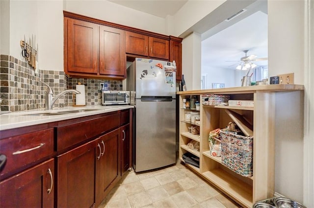 kitchen with tasteful backsplash, light countertops, visible vents, freestanding refrigerator, and a sink
