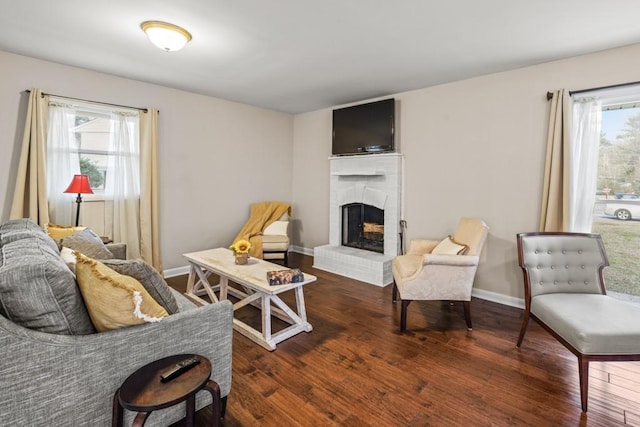 living room featuring a brick fireplace, a healthy amount of sunlight, and dark wood-type flooring