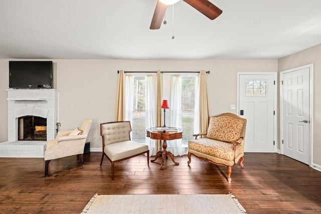 living area with dark hardwood / wood-style flooring, a brick fireplace, and ceiling fan