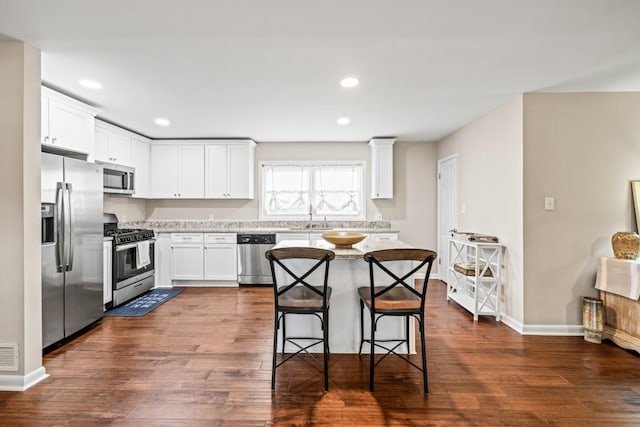 kitchen with appliances with stainless steel finishes, sink, white cabinets, a kitchen bar, and dark wood-type flooring