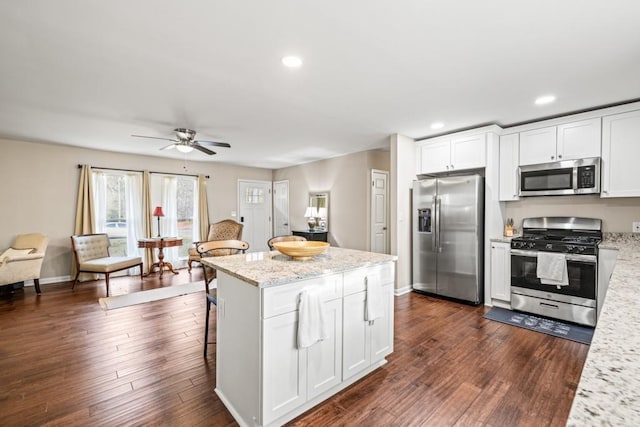 kitchen with stainless steel appliances, a kitchen breakfast bar, light stone counters, white cabinets, and dark hardwood / wood-style flooring