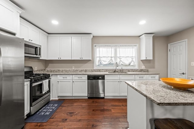 kitchen with sink, appliances with stainless steel finishes, light stone counters, white cabinets, and dark hardwood / wood-style flooring