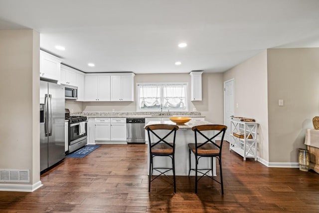 kitchen with sink, stainless steel appliances, dark hardwood / wood-style floors, white cabinets, and a kitchen bar