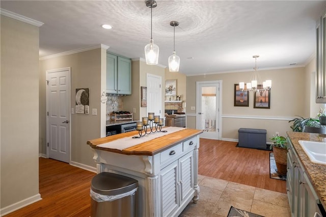 kitchen with light wood finished floors, crown molding, baseboards, butcher block countertops, and pendant lighting