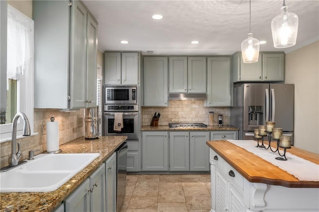 kitchen with a sink, stainless steel appliances, under cabinet range hood, decorative light fixtures, and backsplash