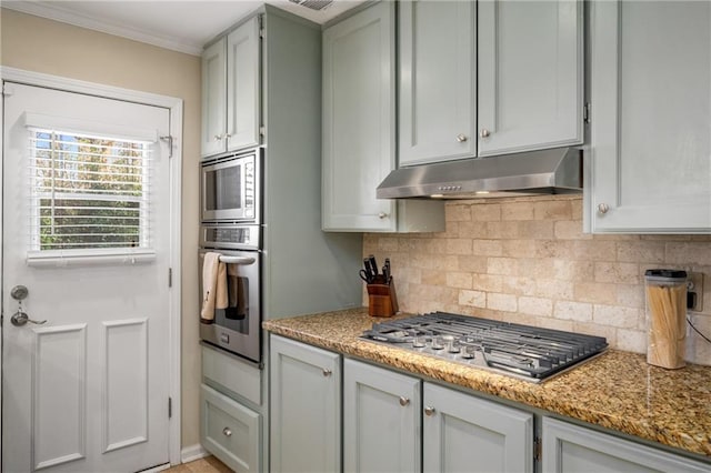 kitchen with light stone counters, ornamental molding, under cabinet range hood, appliances with stainless steel finishes, and backsplash